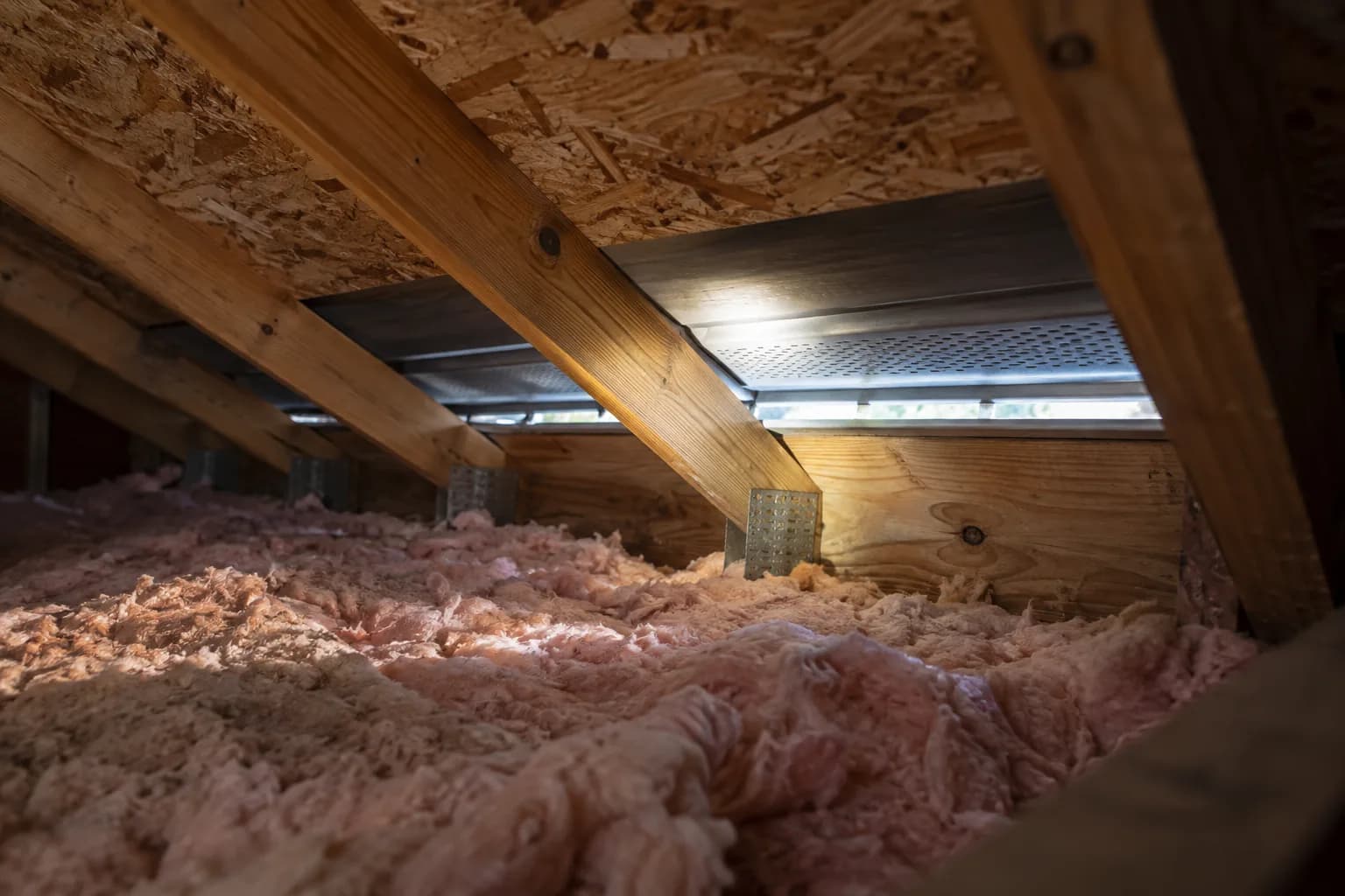 Attic rafters, insulation and a soffit opening illuminated for inspection